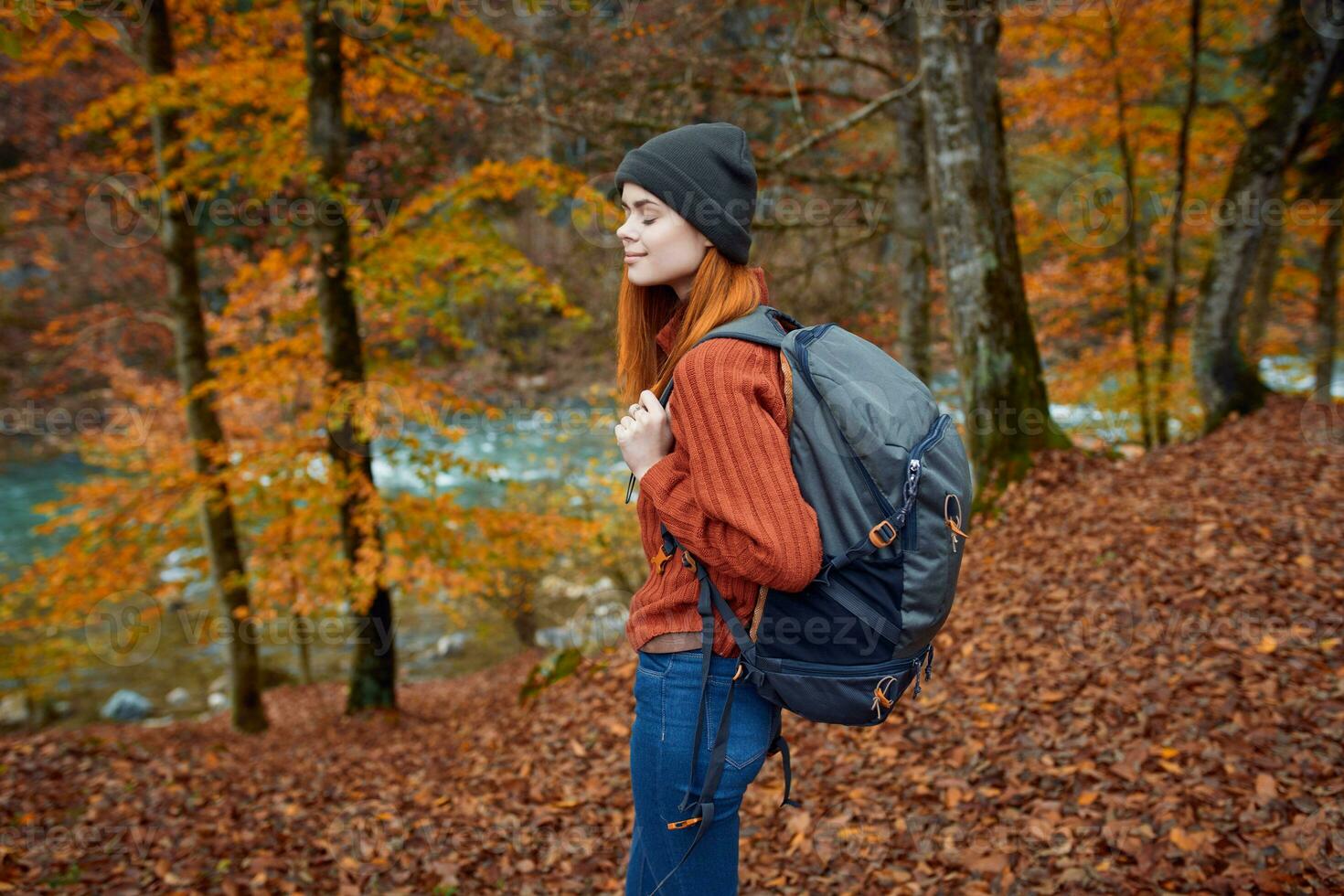 woman with backpack walking in the autumn park near the river in nature side view photo
