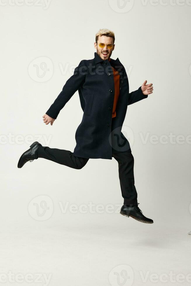 handsome blond man jumped up in black coat and pants boots fashion trend of the season photo
