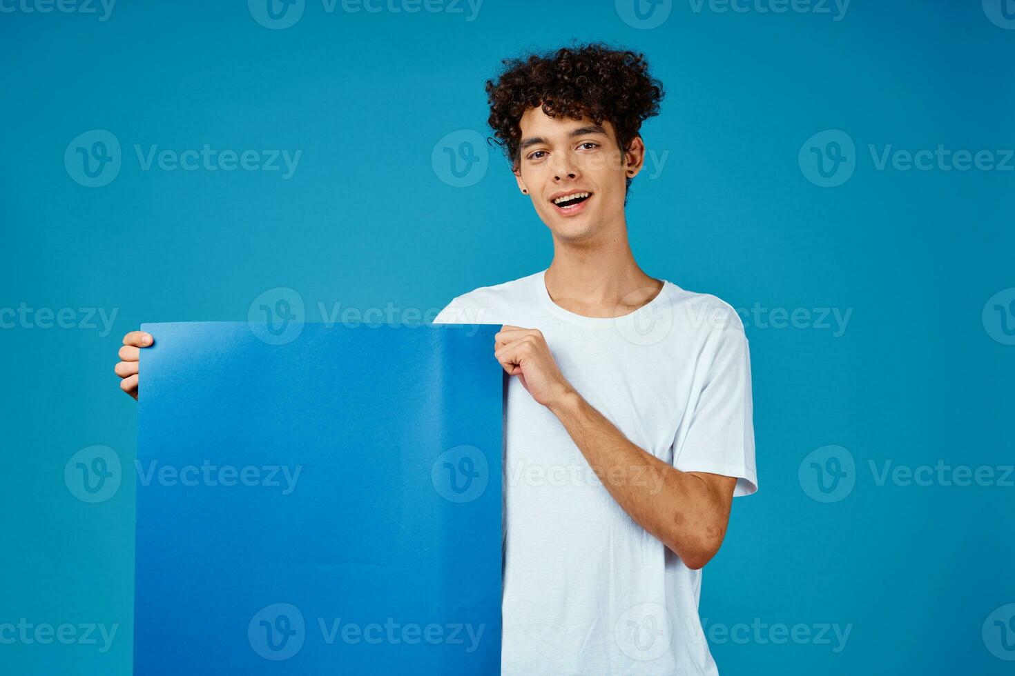 guy in a white t-shirt holding a poster mockup advertising blue background photo