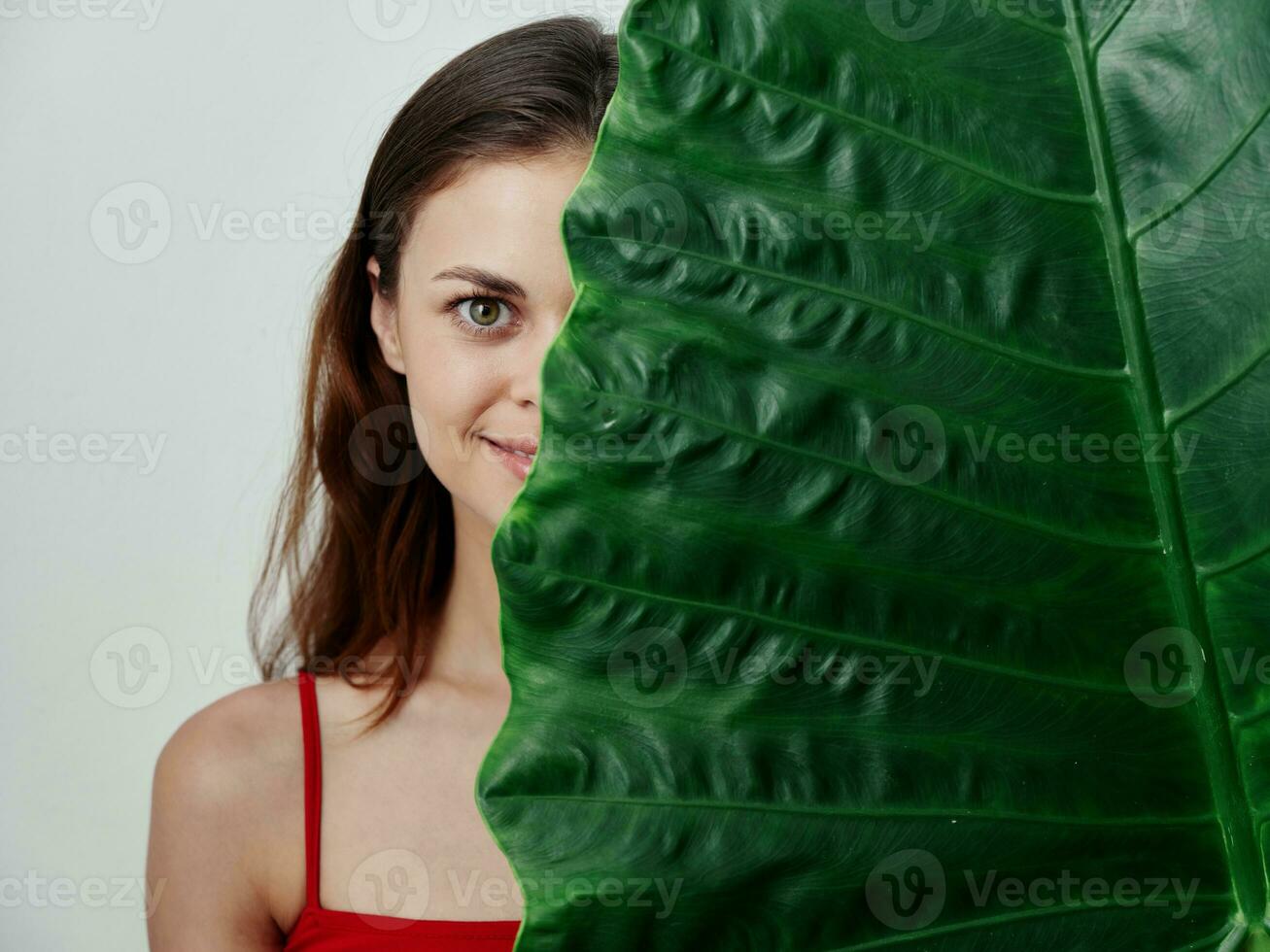 smiling woman in a swimsuit peeking out from behind a green leaf studio photo