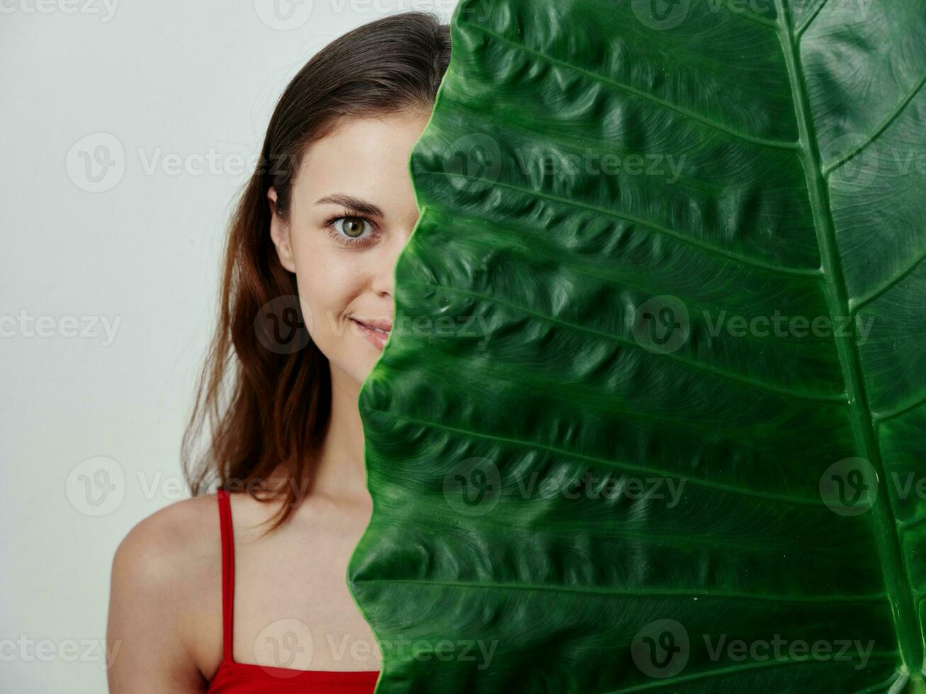 sonriente mujer en un traje de baño echar un vistazo fuera desde detrás un verde hoja estudio foto