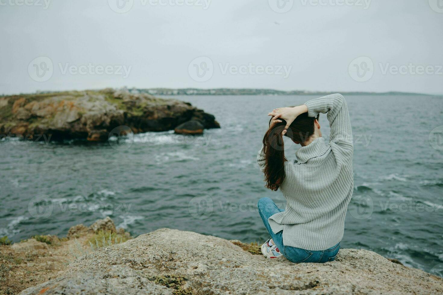 woman sitting by the sea holding her hair landscape back view photo
