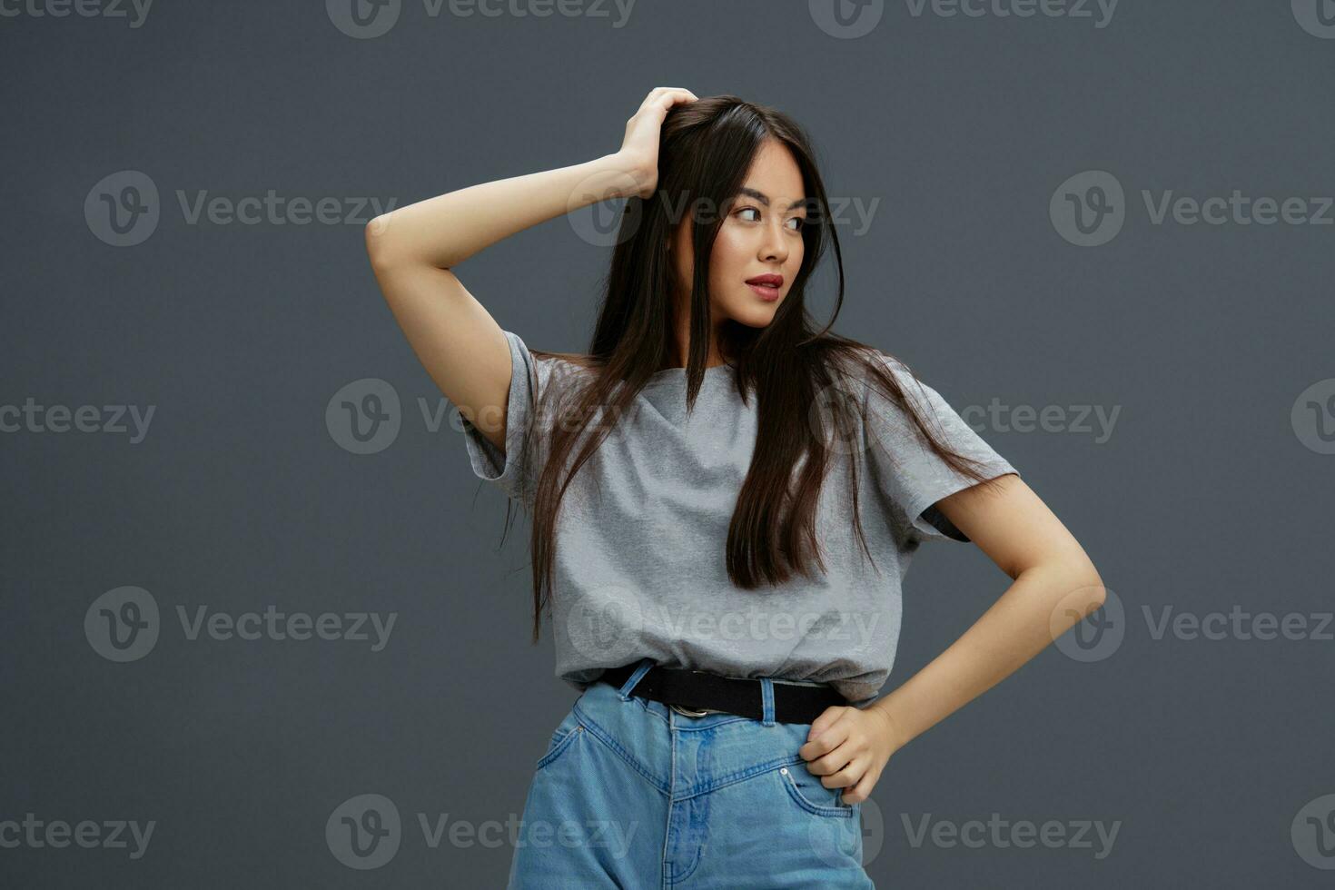 Brunette with long hair in a gray T-shirt gesturing with hands Gray background photo