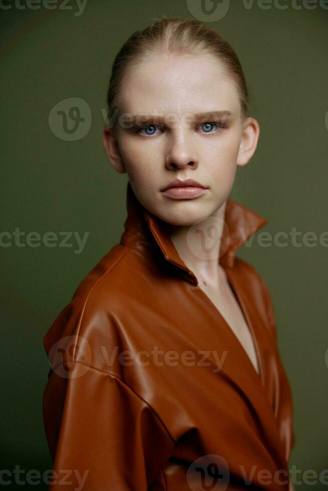 Elegant fashionable young blonde girl with blue eyes with evening makeup in a leather dress looks at the camera posing isolated for banner design. Studio portrait on a green background. Makeup concept photo