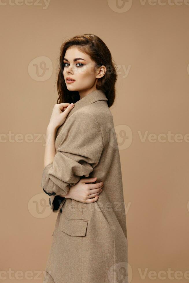woman in coat hugs herself with hands on beige background hairstyle makeup model photo
