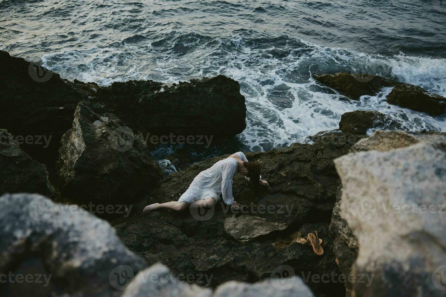 beautiful young woman in a secluded spot on a wild rocky coast in a white dress unaltered photo