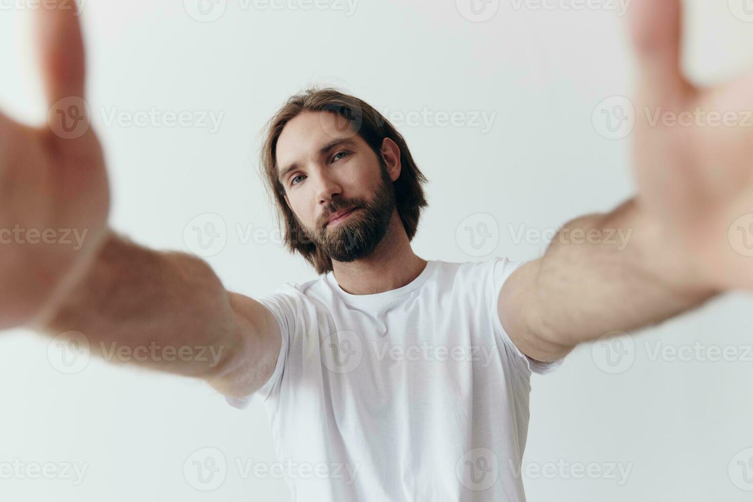 contento adulto hombre con un barba sonrisas y tira el cocinar dentro el cámara escuchando a música en auriculares en un afligido camiseta en un blanco aislado antecedentes foto