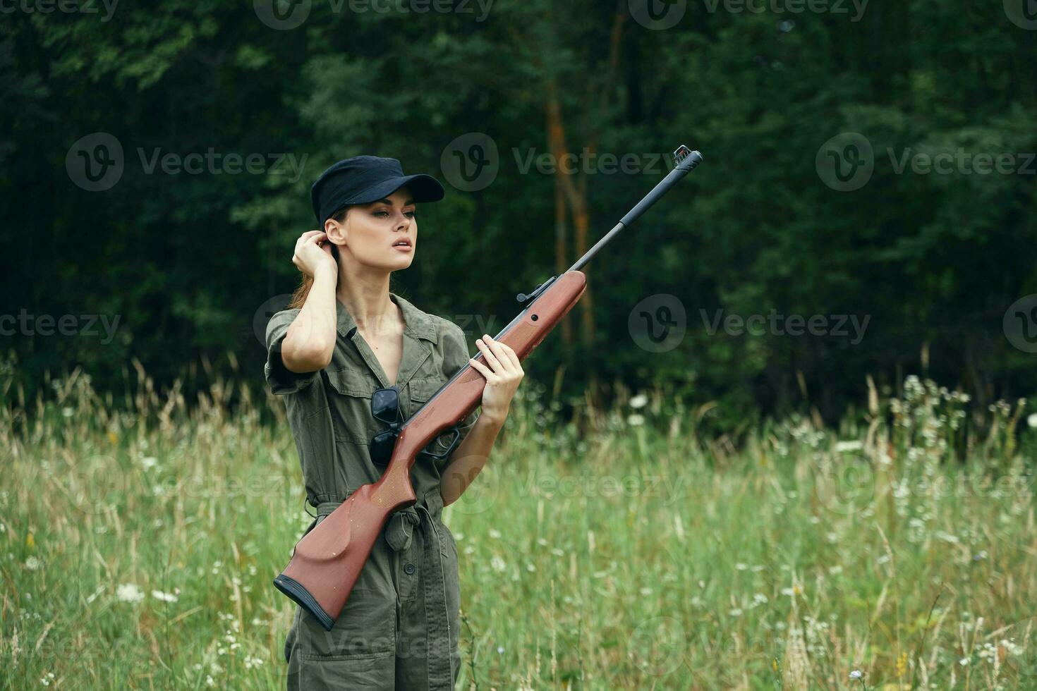 Woman on nature holding a gun in his hands black travel cap green overalls photo
