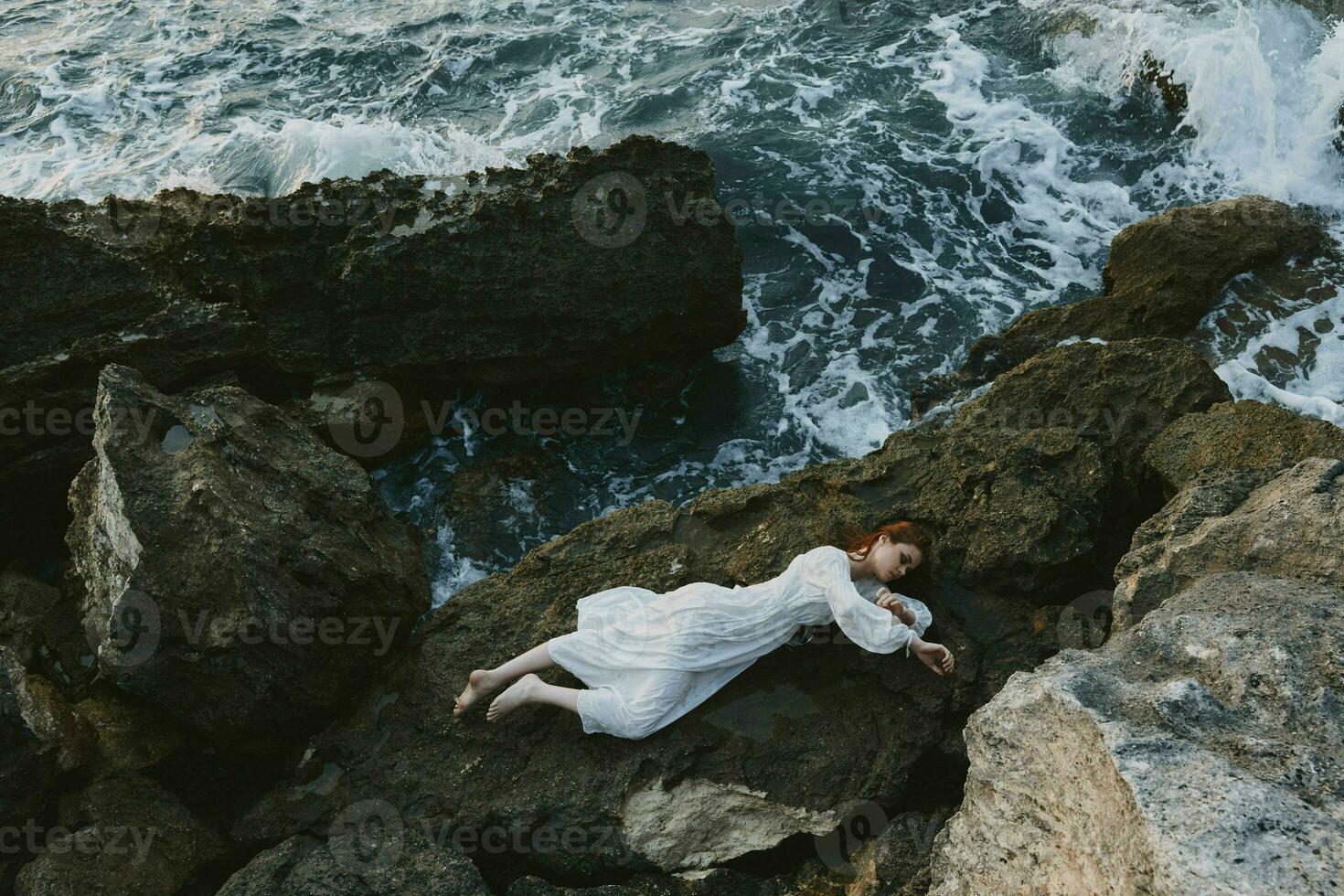 hermosa mujer en un aislado Mancha en un salvaje rocoso costa en un blanco vestir ver desde encima foto