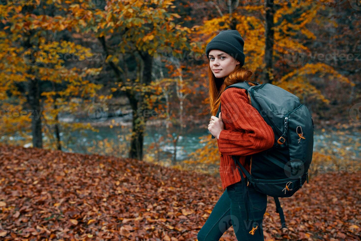 fallen leaves in the park in autumn and the river in the background woman tourist with a backpack travel photo