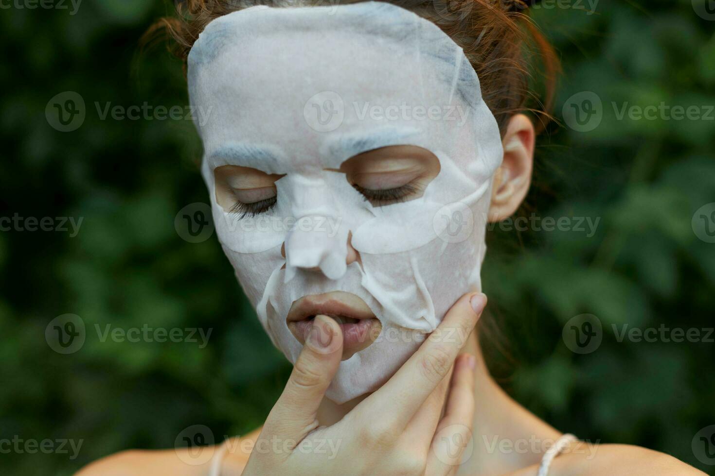 Portrait of a woman anti-aging mask holds a finger near the lips and closed eyes bare shoulders leaves in the background photo