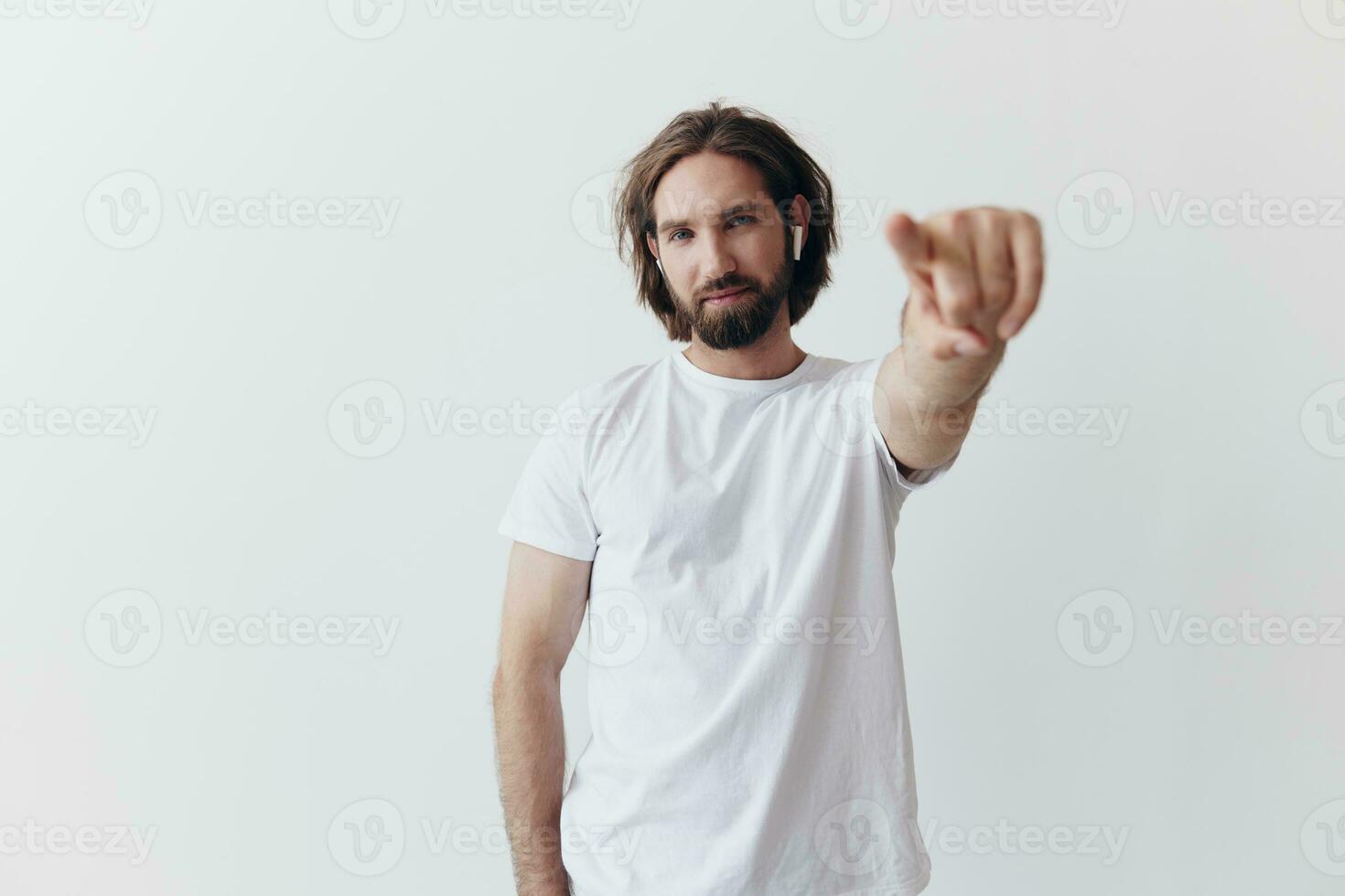 happy man listening to music and smiling in a white t-shirt on a white background and pointing a finger at the screen at the camera photo