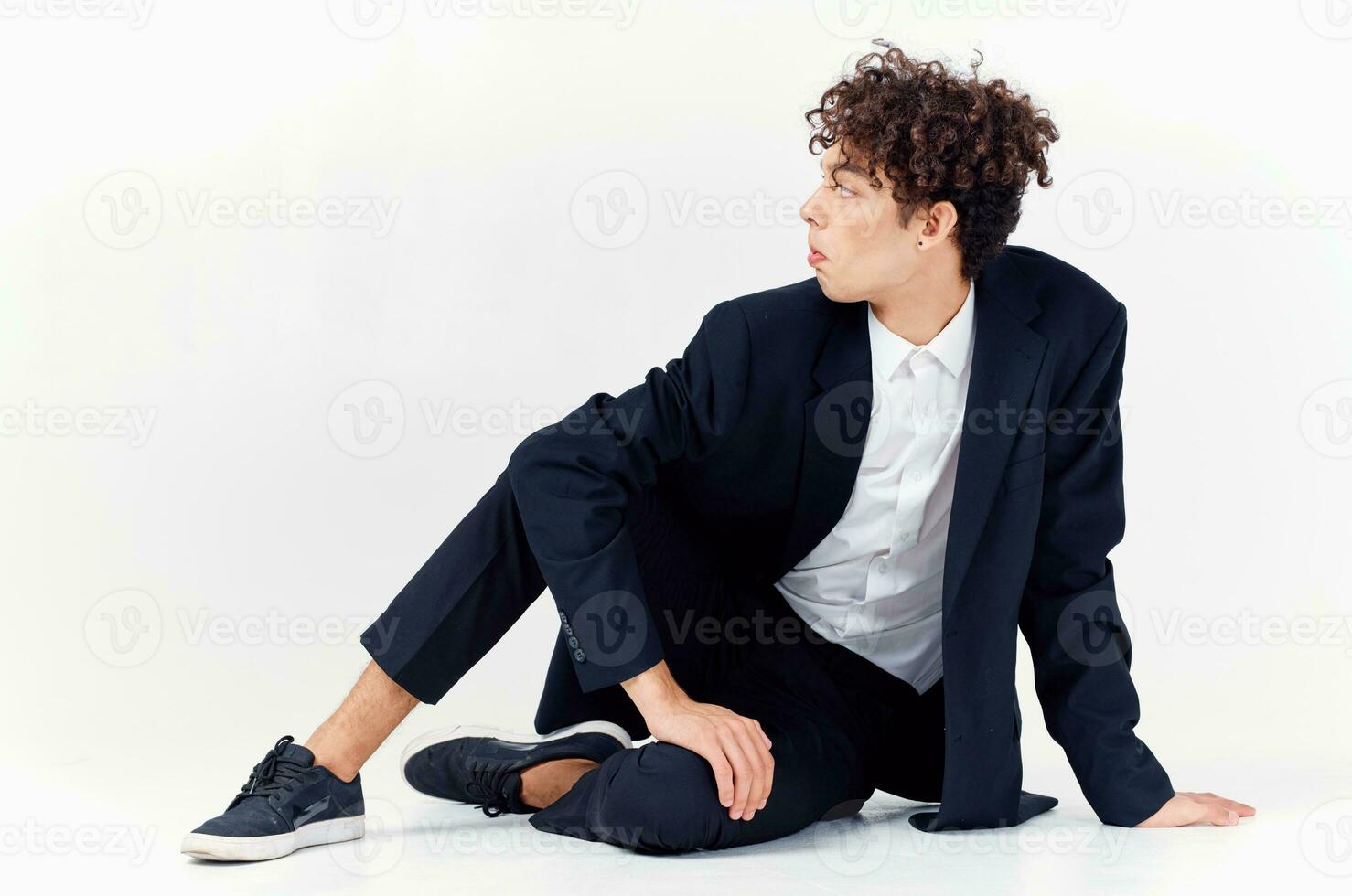 fashionable guy in a suit and sneakers sitting on the floor in a bright room curly hair model photo