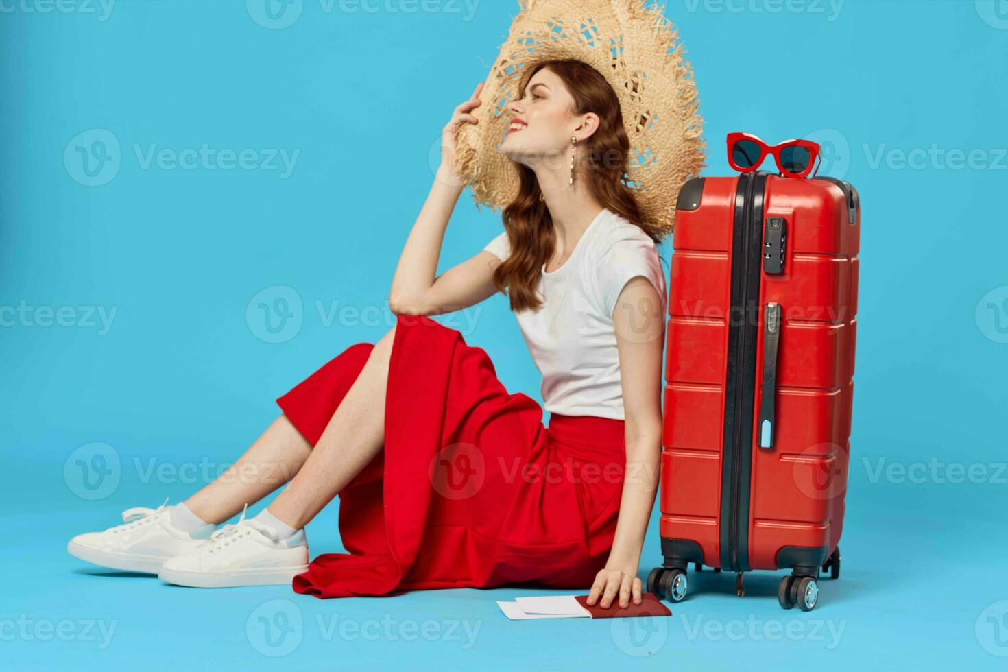 cheerful woman in hat sitting on the floor red suitcase passenger isolated background photo