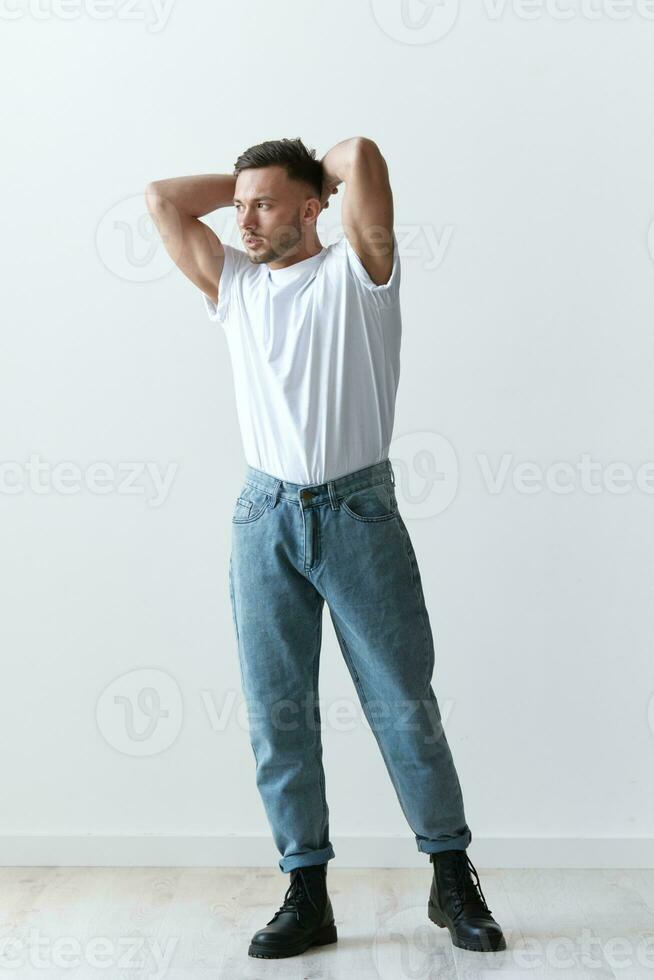 Full body shot of handsome serious tanned man guy in basic t-shirt holds hand behind head posing on white background. Fashion Style New Collection Offer. Copy space for ad. Modeling snapshots photo
