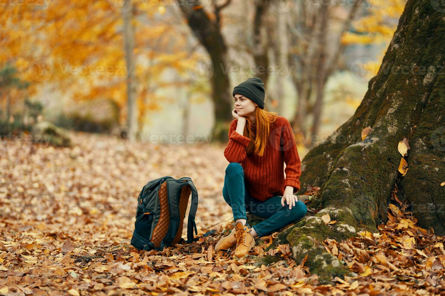 mujer cerca árbol y mochila para viaje caído hojas otoño bosque foto