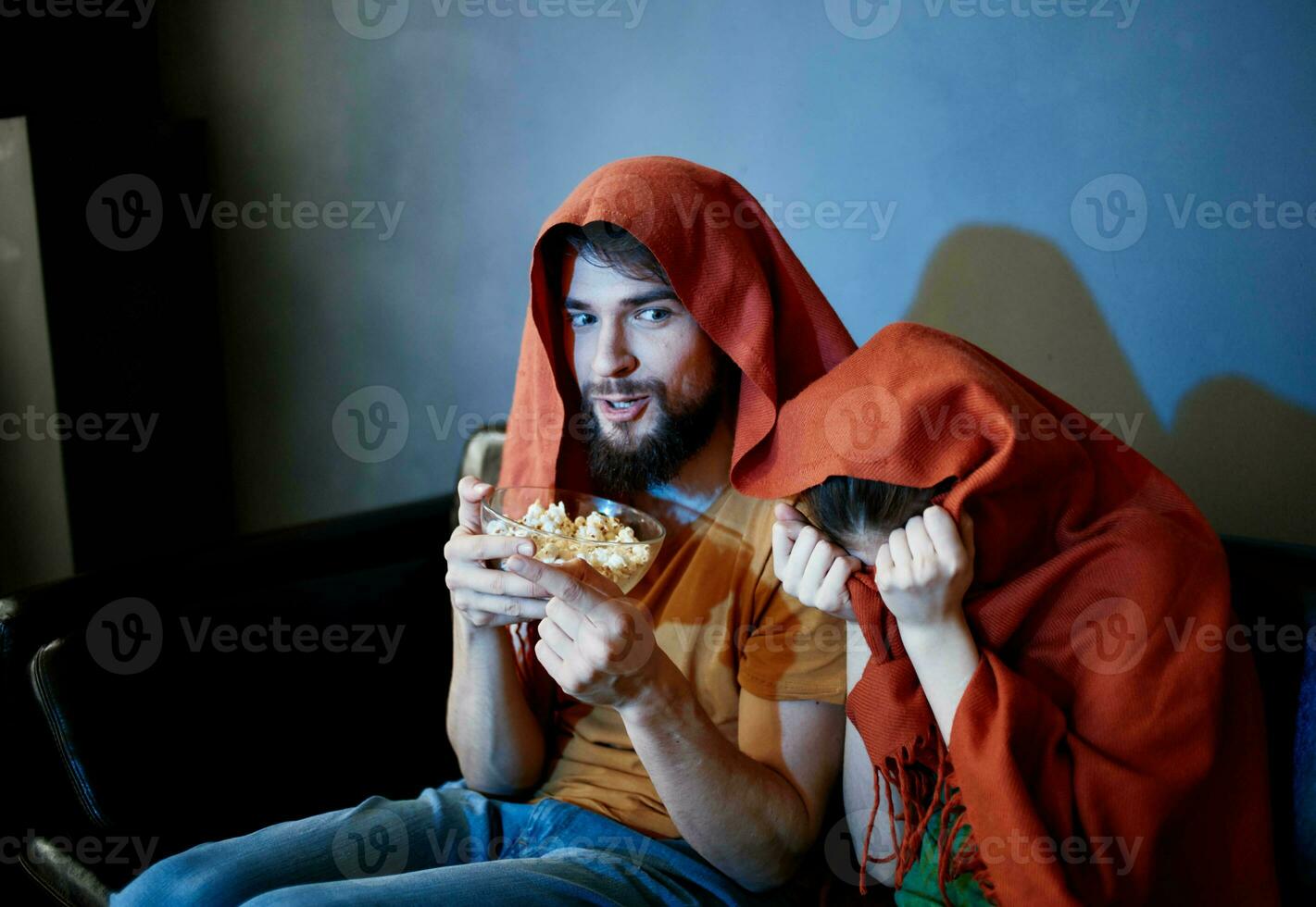 asustado mujer con un rojo tartán en su cabeza y un hombre con un plato de palomitas de maiz en un oscuro habitación foto