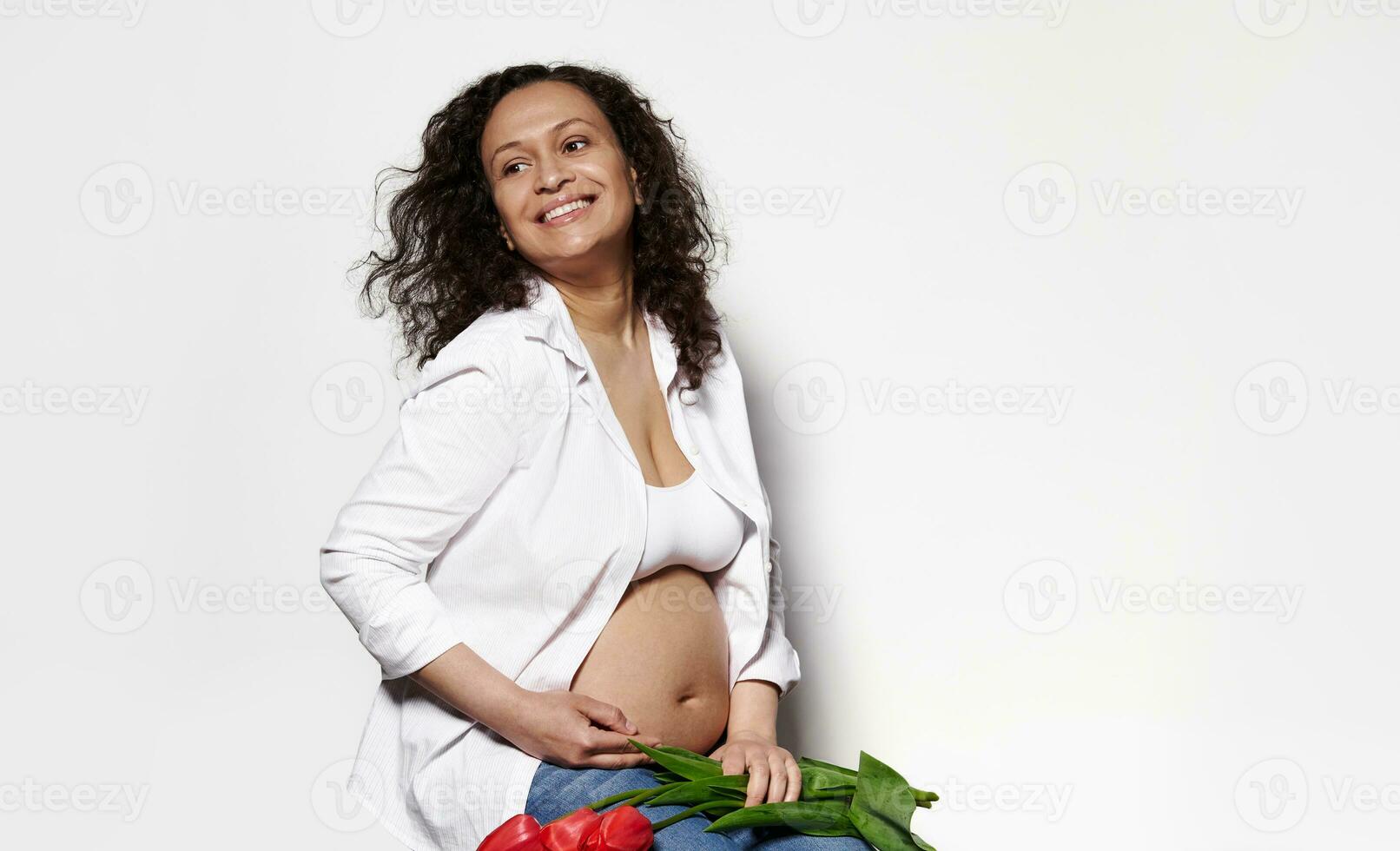 hermosa embarazada mujer sonrisas, acariciando barriga, expresando positivo emociones desde el embarazo, aislado blanco antecedentes foto