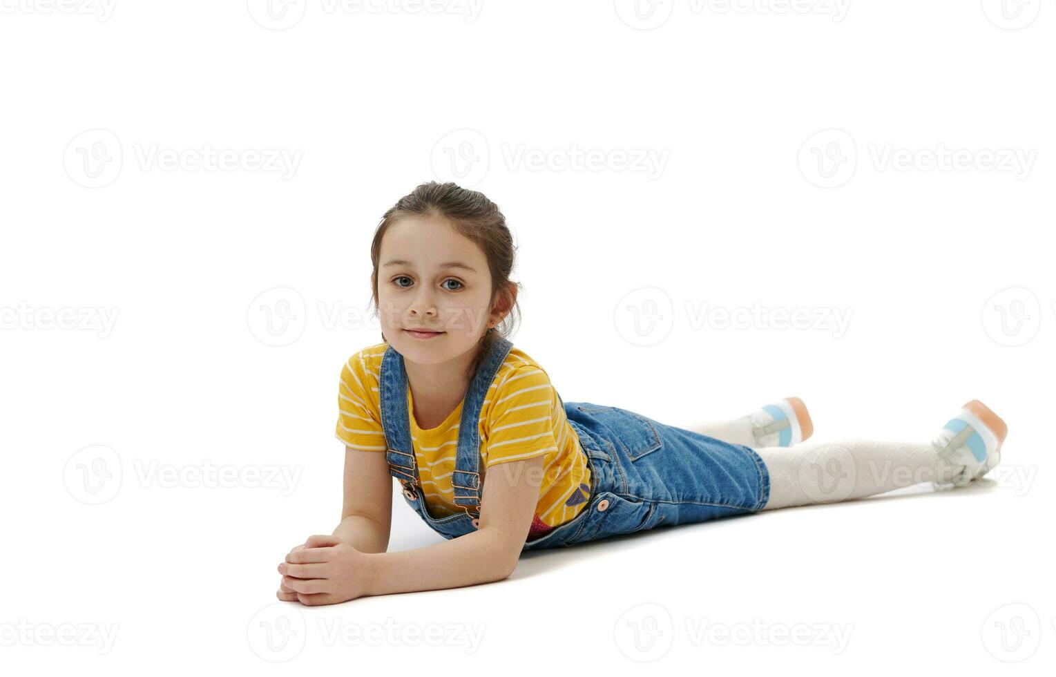 Horizontal full length portrait of Caucasian child girl lying on belly, looking confidently at camera, white background photo