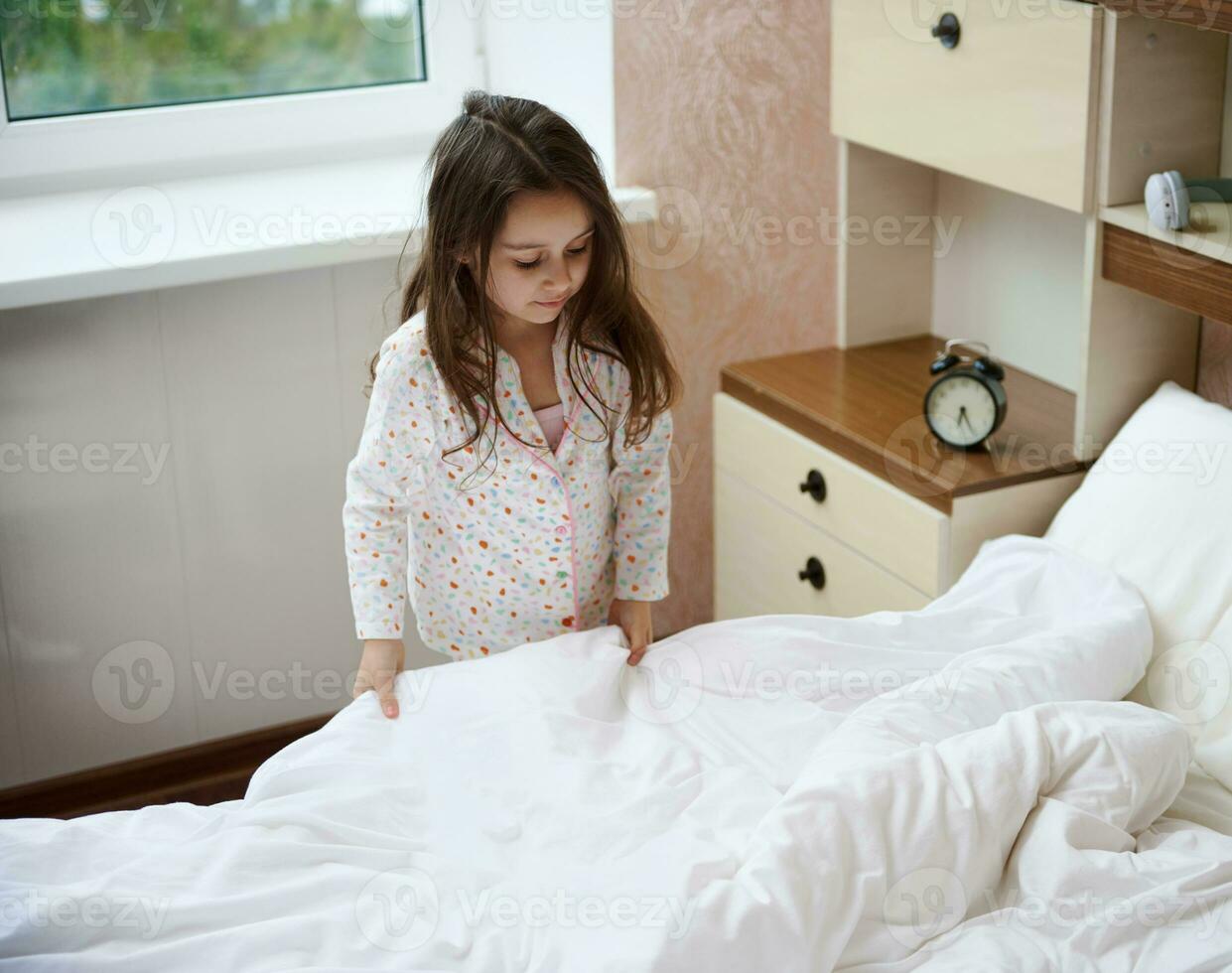 Little girl in pajama, folding her bed and cleans the room after waking up in the morning. Teaching children to order photo