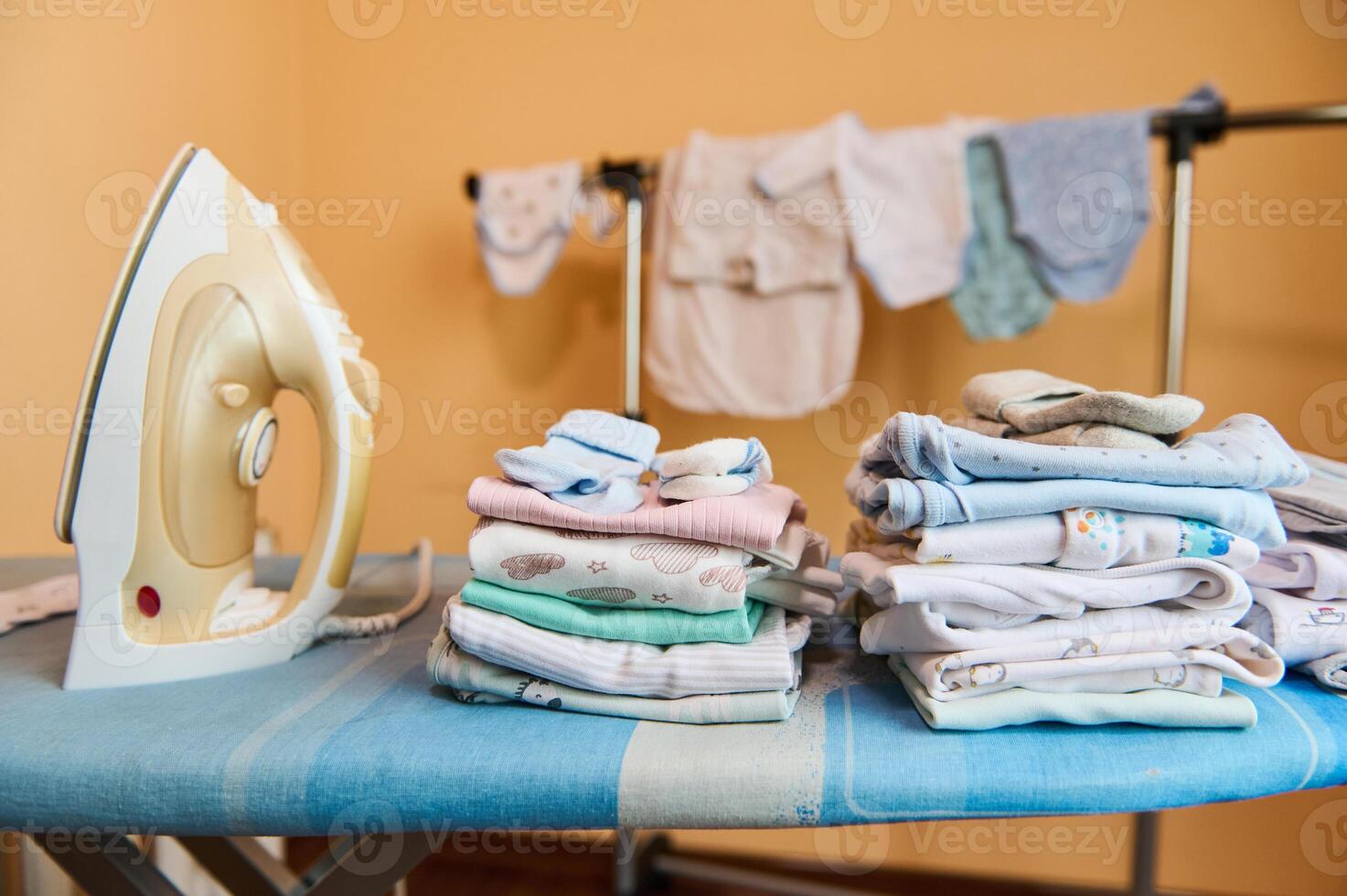 Clean laundered baby clothes ironed and folded in stack near steam iron on an ironing board in dressing room or laundry photo