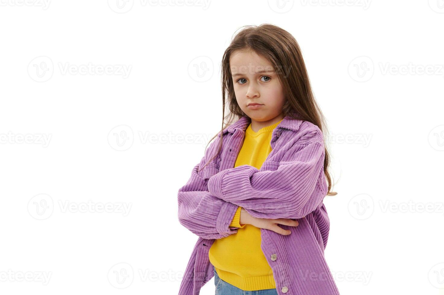 Naughty mischievous little girl pouting lips in resentment, looking at camera with displeased look and her arms folded photo