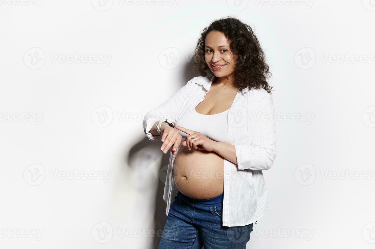 medio Envejecido embarazada mujer cheques móvil aplicación en inteligente mirar, cuenta bebé movimientos, sonriente a cámara, aislado en blanco foto
