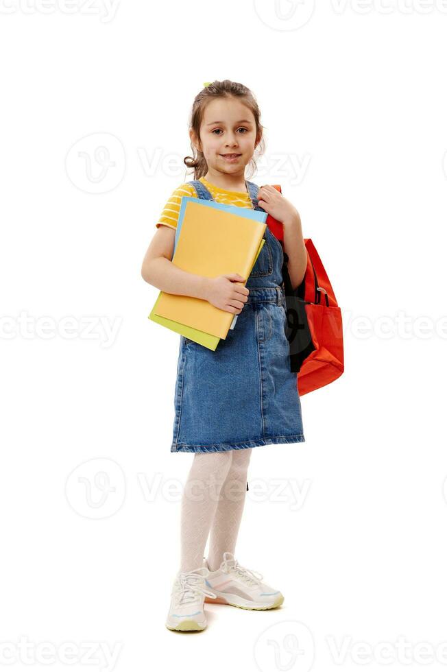 Portrait of Caucasian beautiful little girl, school kid holding backpack and studying books, isolated white background photo