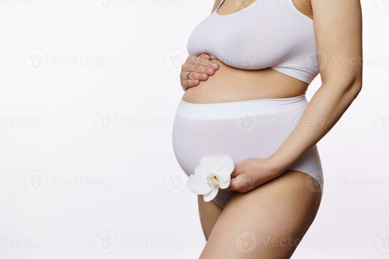 de cerca embarazada mujer participación un blanco floreciente orquídea flor y suavemente acariciando su barriguita, aislado antecedentes foto