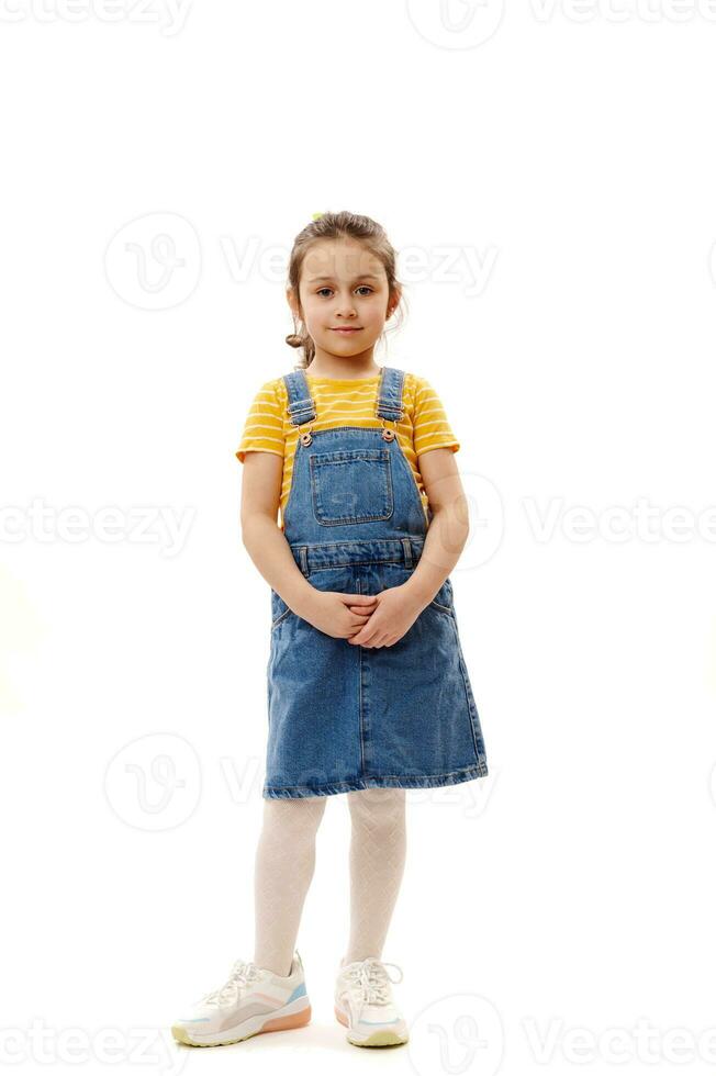 Full length portrait of a beautiful little child girl in denim clothes, looking at camera isolated over white background photo