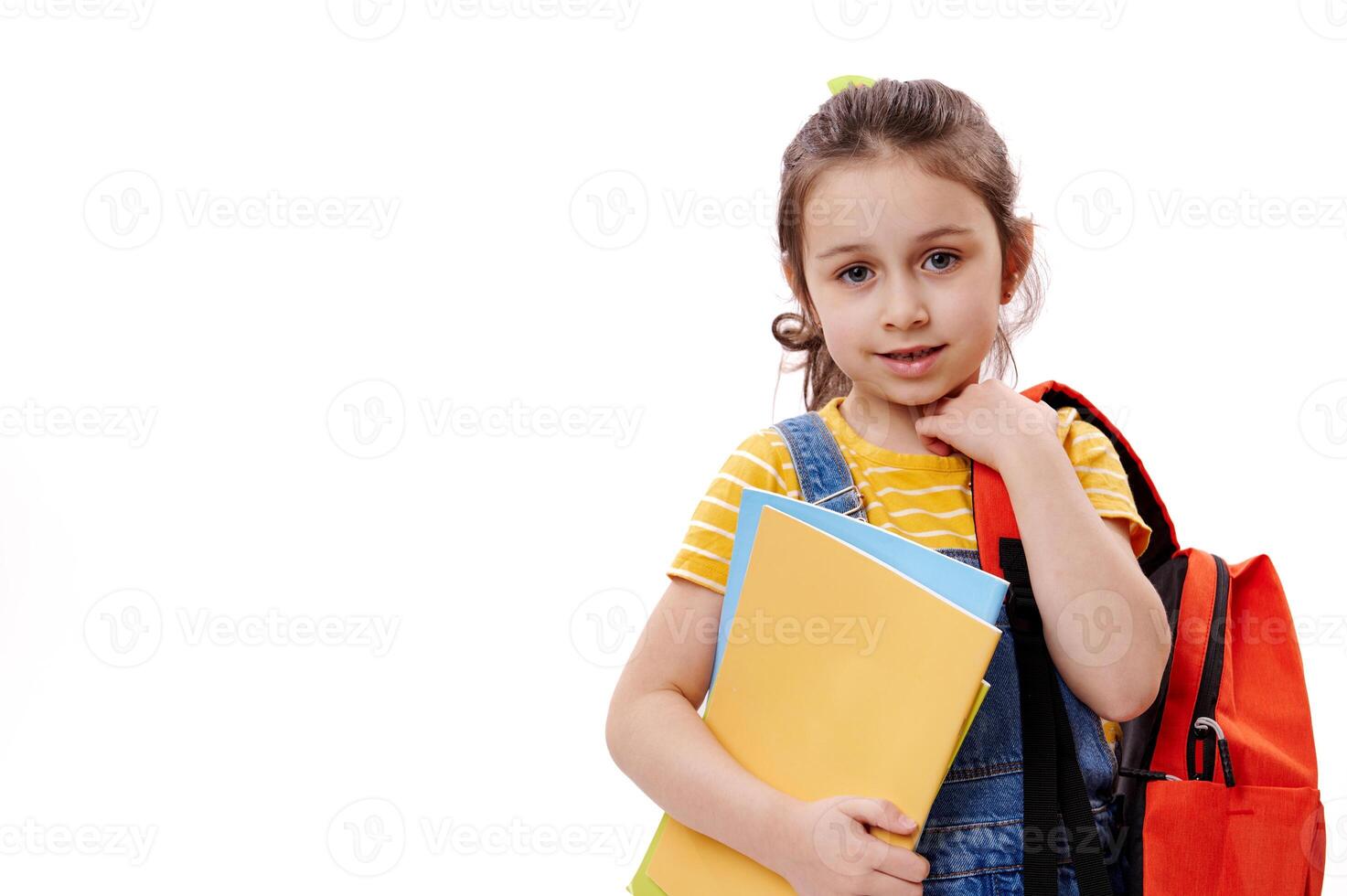 Horizontal portrait of Caucasian first grader schoolgirl, holding books, smiling at camera, isolated on white background photo