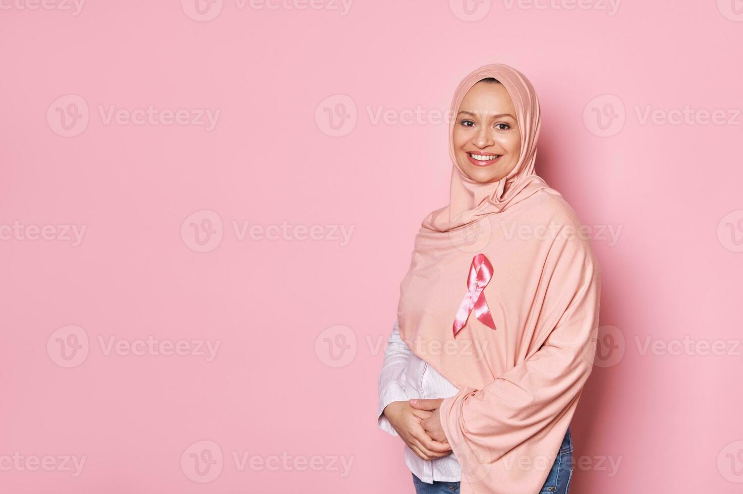 Muslim pregnant woman in pink hijab, wearing satin ribbon, show support for cancer patients. Breast Cancer Awareness Day photo