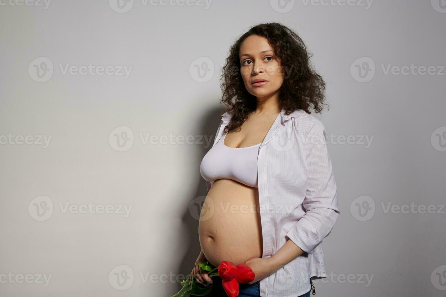 Attractive sexy African American pregnant woman with red tulips on belly. Pregnancy 24 weeks. 6 month. Maternity concept photo