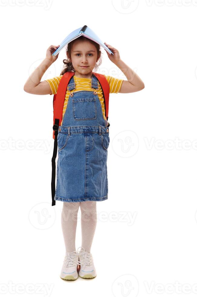 Full length first grade student holding open book above her head, smiles looking at camera, isolated on white background photo