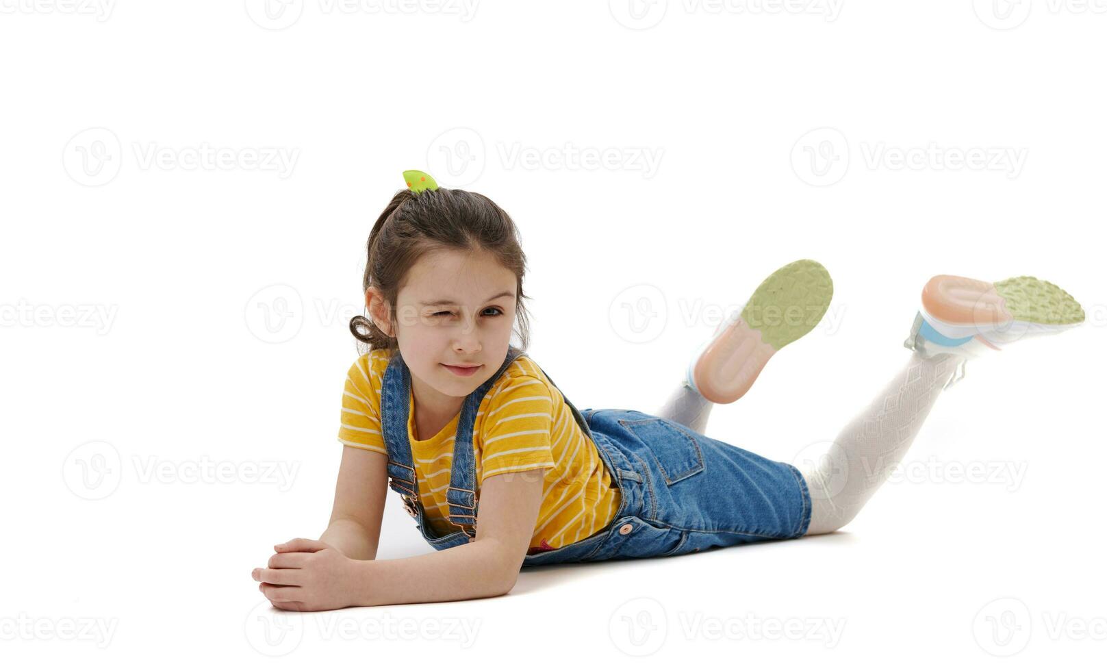 Adorable Caucasian little kid girl winking looking at camera, lying on while background with free ad space. photo