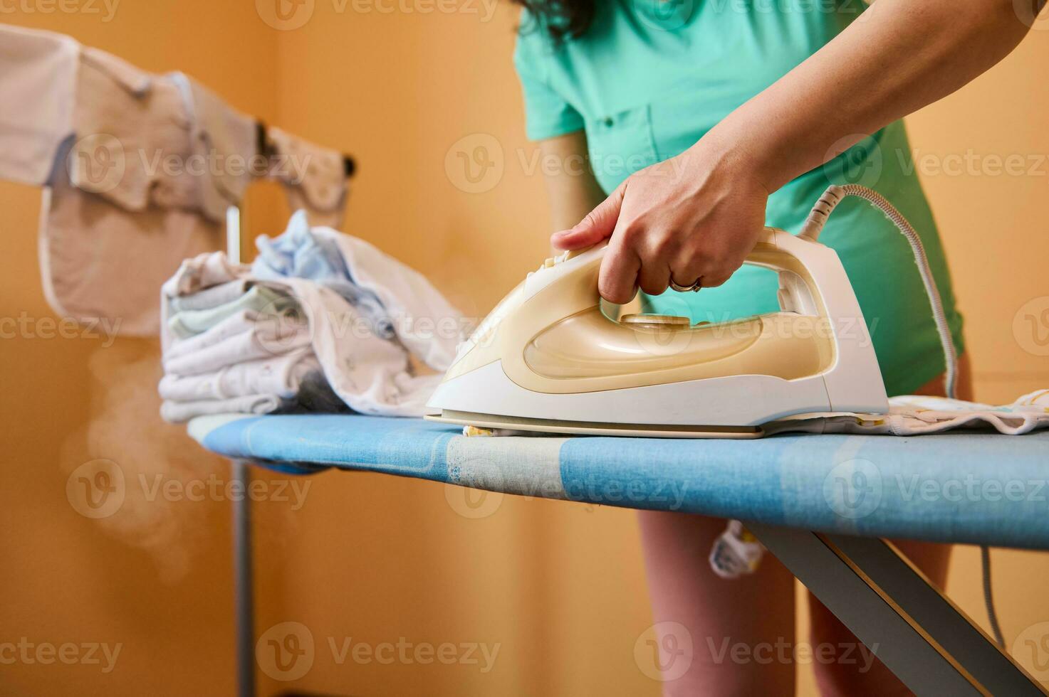 Closeup of hand of a pregnant woman holding electric steam iron, ironing, steaming laundered clean newborn baby clothes photo