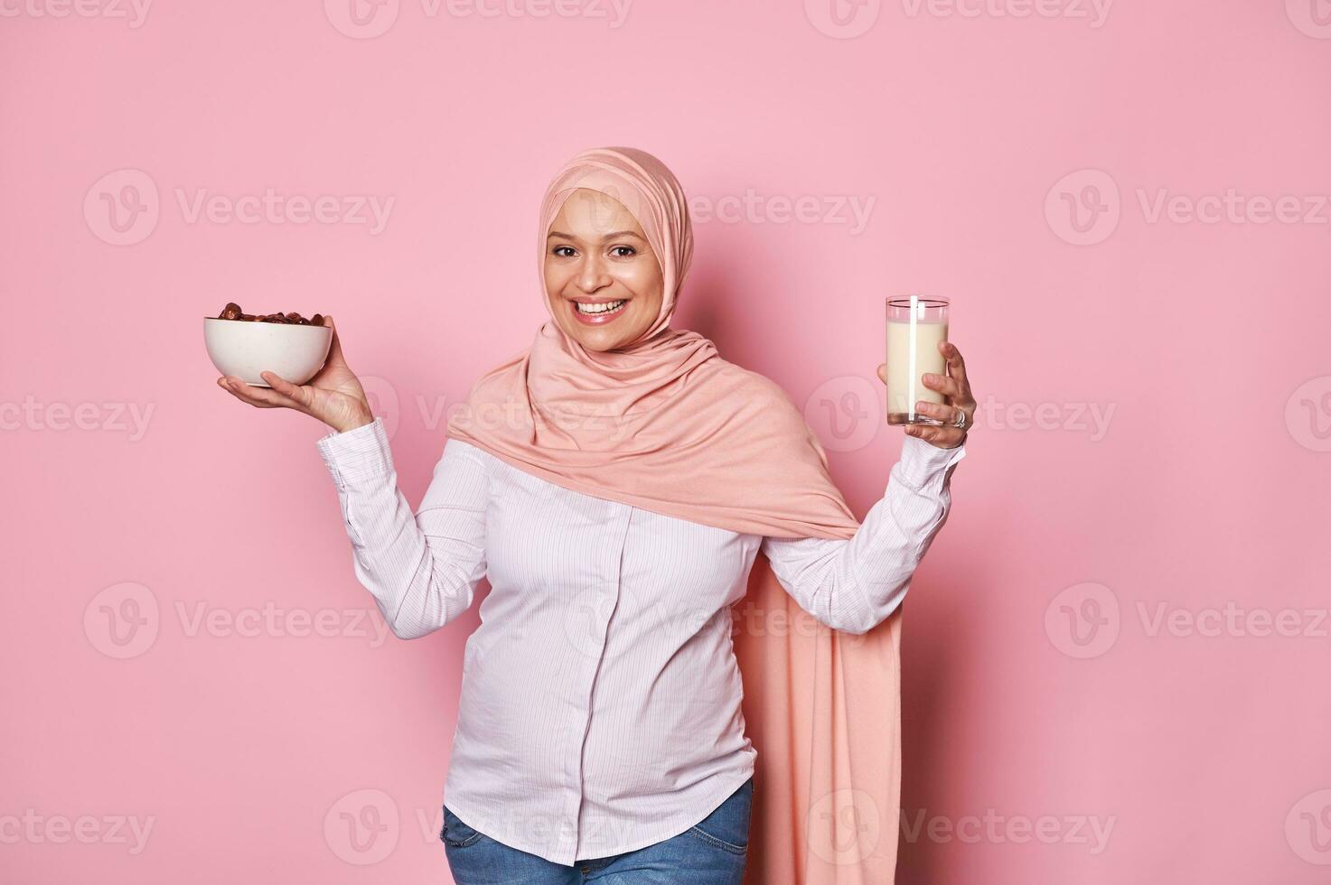 maravilloso árabe musulmán mujer en rosado hiyab, sostiene sano desayuno en Ramadán - cuenco con dulce fechas y vaso con Leche foto