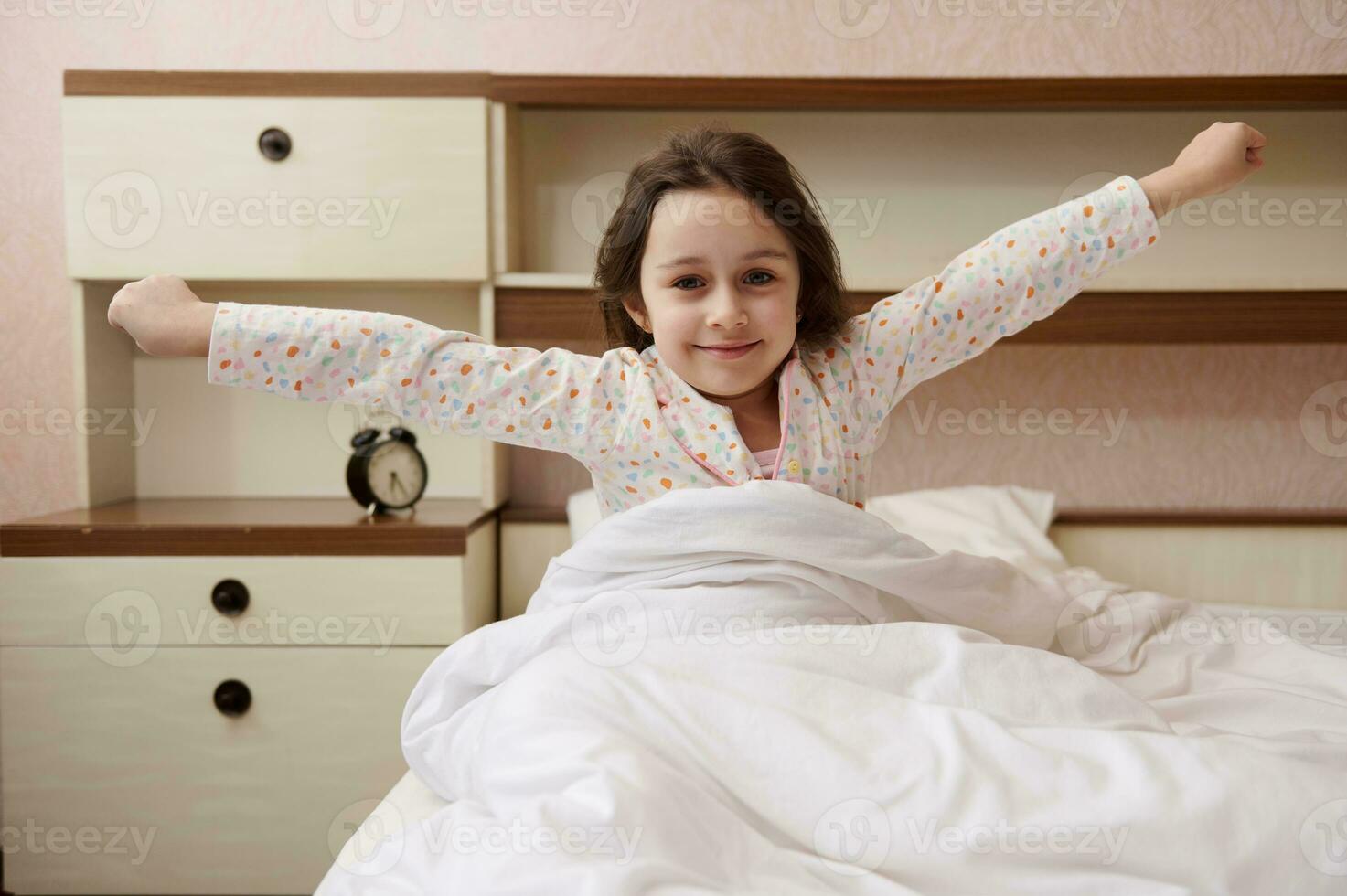 Adorable baby girl in stylish pajamas, waking up stretching in the morning in her bedroom at home photo