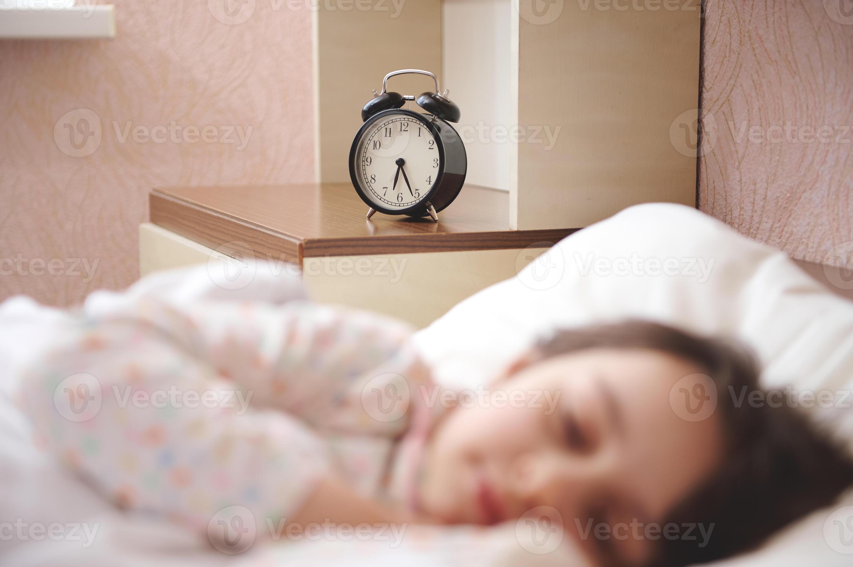 Focus on black alarm clock showing half past six, on bedside nightstand