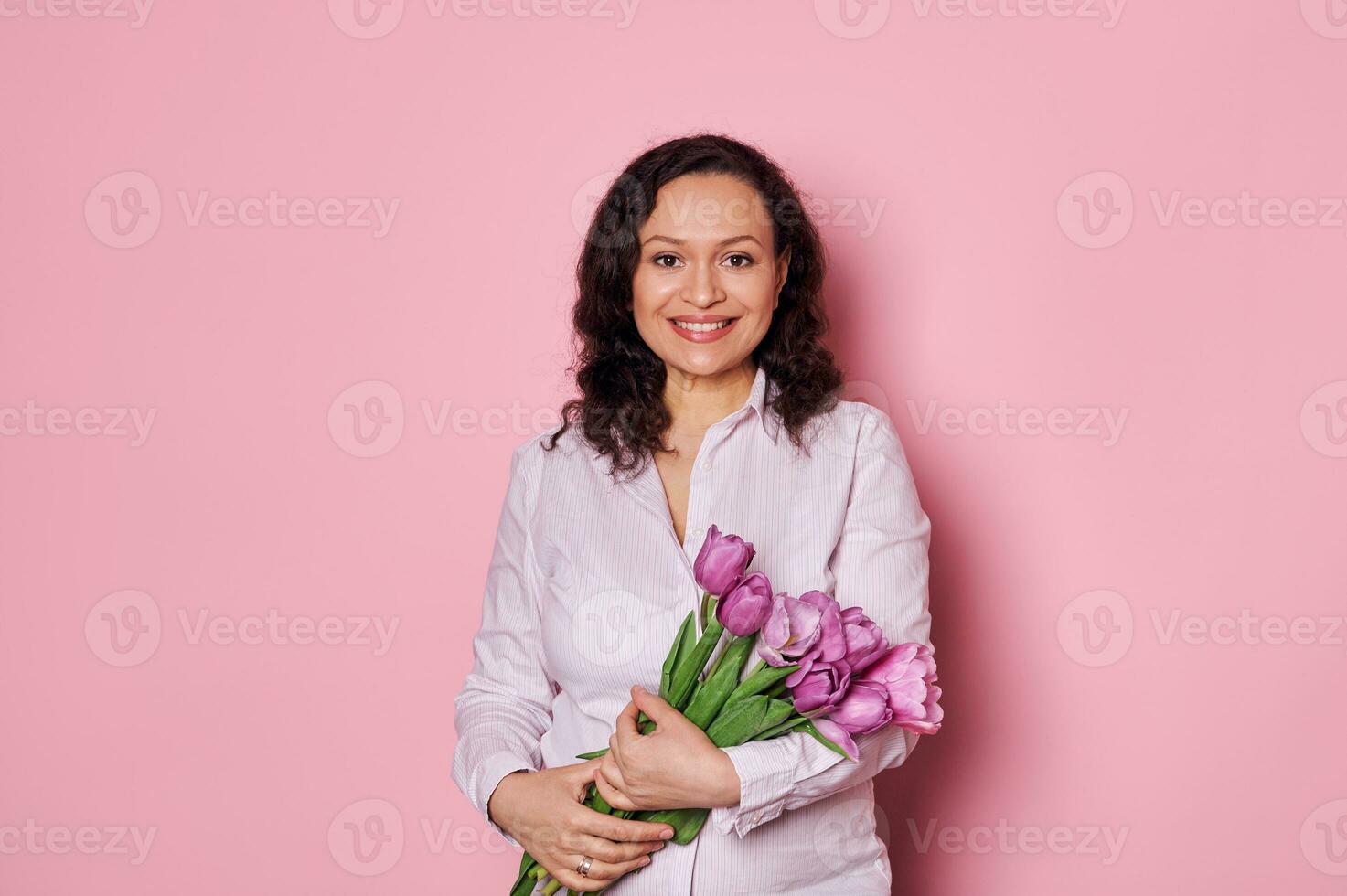 atractivo embarazada mujer, participación manojo de púrpura tulipanes, aislado en rosado. contento de madre, internacional De las mujeres día foto