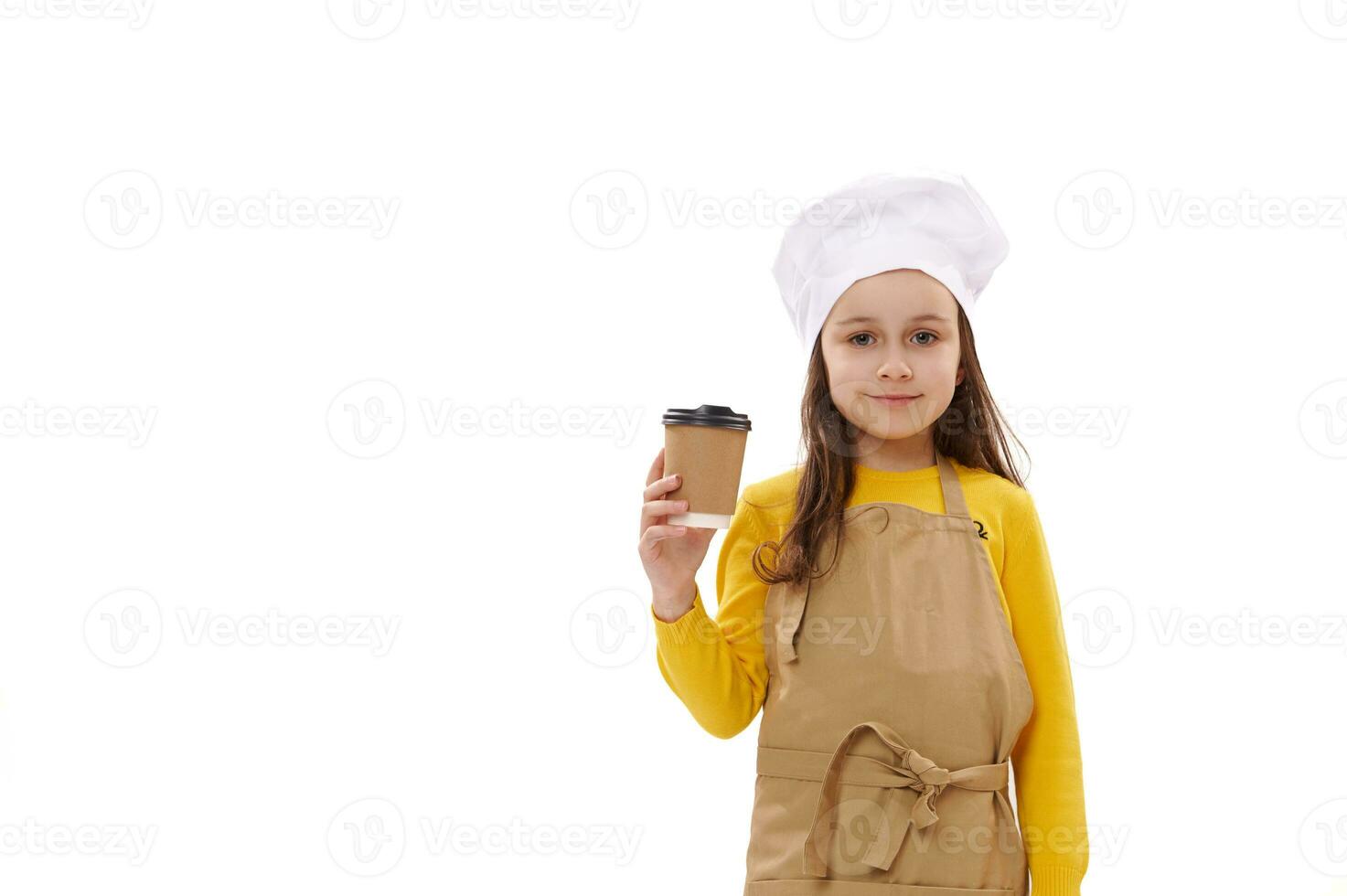Caucasian kid girl in chef's hat and kitchen apron, holds takeaway drink in disposable paper cup. Food delivery service photo
