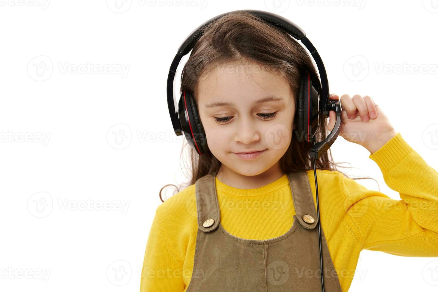 Mischievous little child girl, primary school student, first grader with headphones, smiling, white isolated background photo