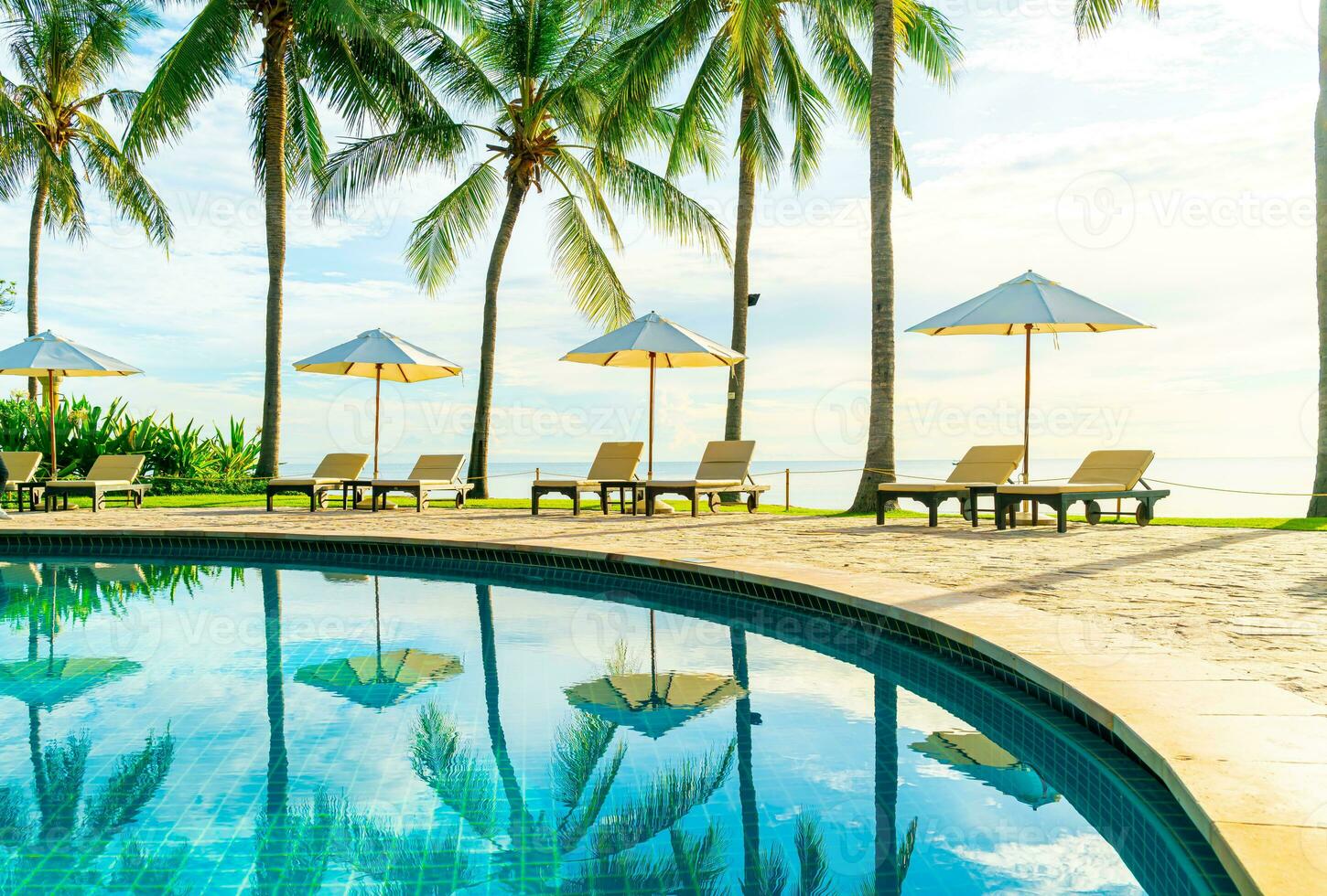 Hermosa sombrilla de lujo y una silla alrededor de la piscina al aire libre en el hotel y resort con palmera de coco en el cielo al atardecer o al amanecer foto
