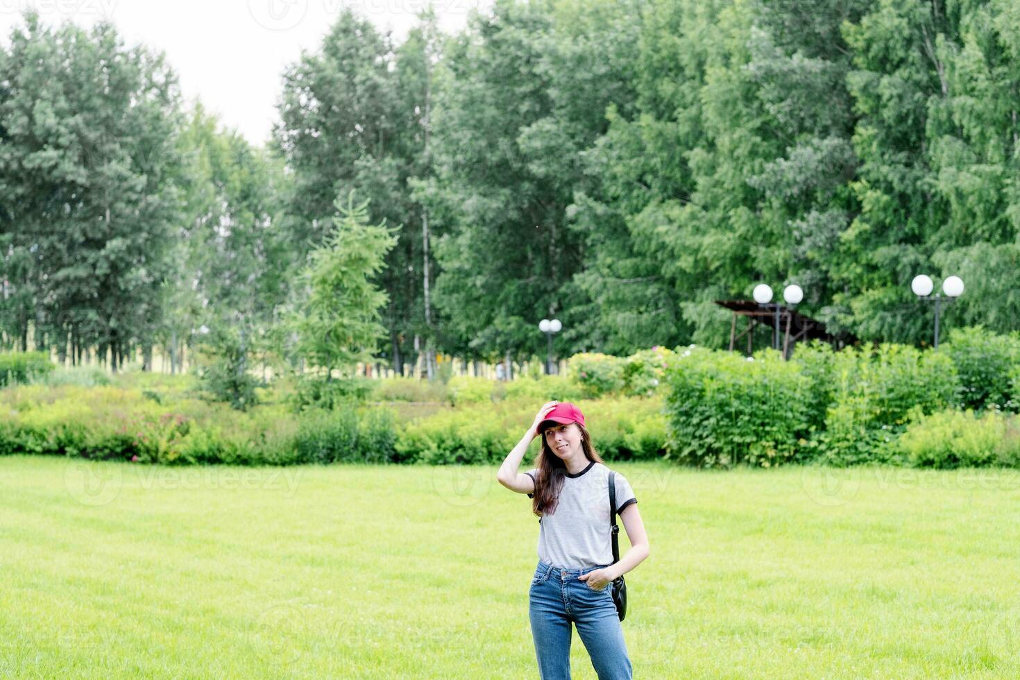 a girl in a gray T-shirt and a red cap on a background of greenery, in the park, copy space photo