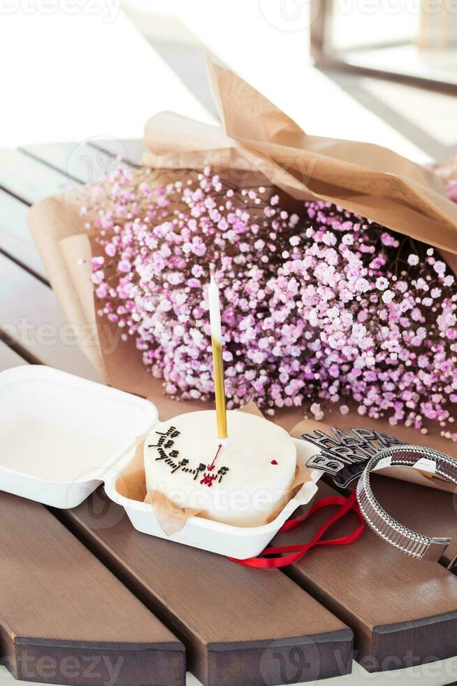 Bento cake with a candle with a bouquet of pink gypsophila on a wooden table, in a cafe. Little surprise for a girl's birthday photo