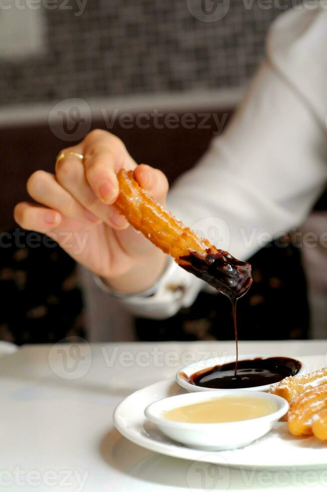 una mano sumergiendo churros españoles en salsa de chocolate negro caliente foto