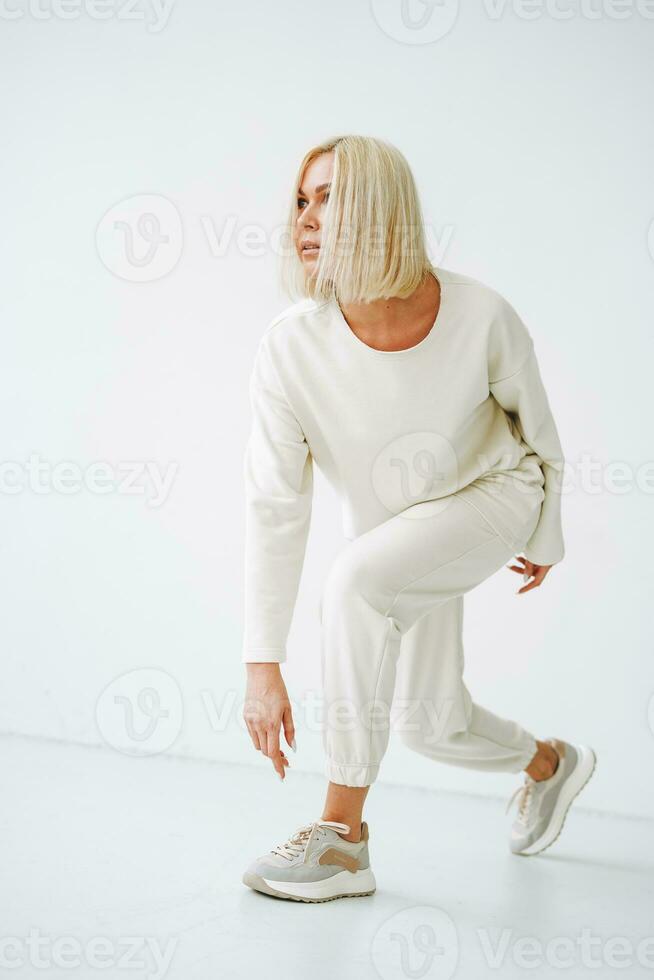 Full length portrait of smiling young blonde woman in sportswear on background of white wall photo