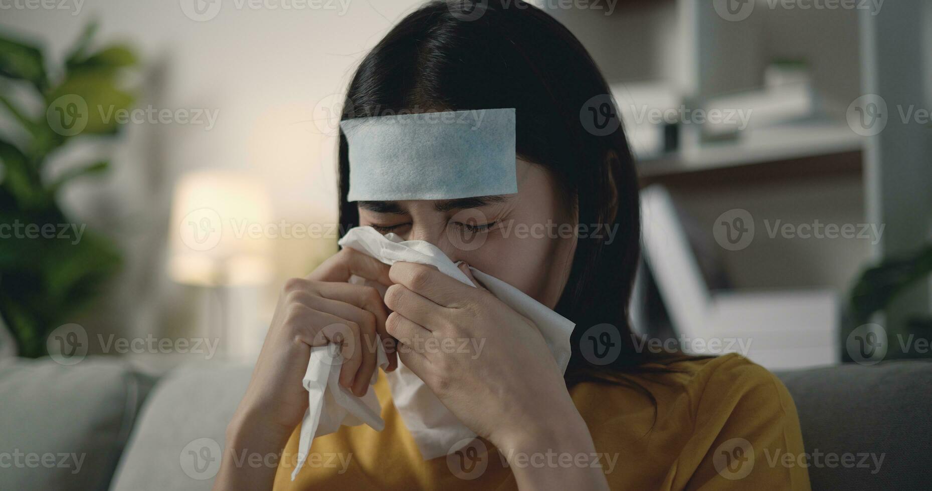 joven asiático mujer sufrimiento desde gripe con un para reducir la fiebre parche en su frente foto
