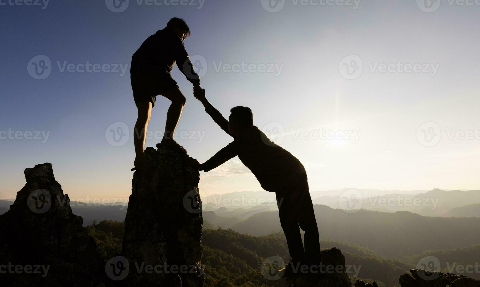 silueta de dos masculino caminantes alpinismo arriba montaña acantilado y uno de ellos dando Ayudar mano. personas Ayudar y, equipo trabajo concepto. foto