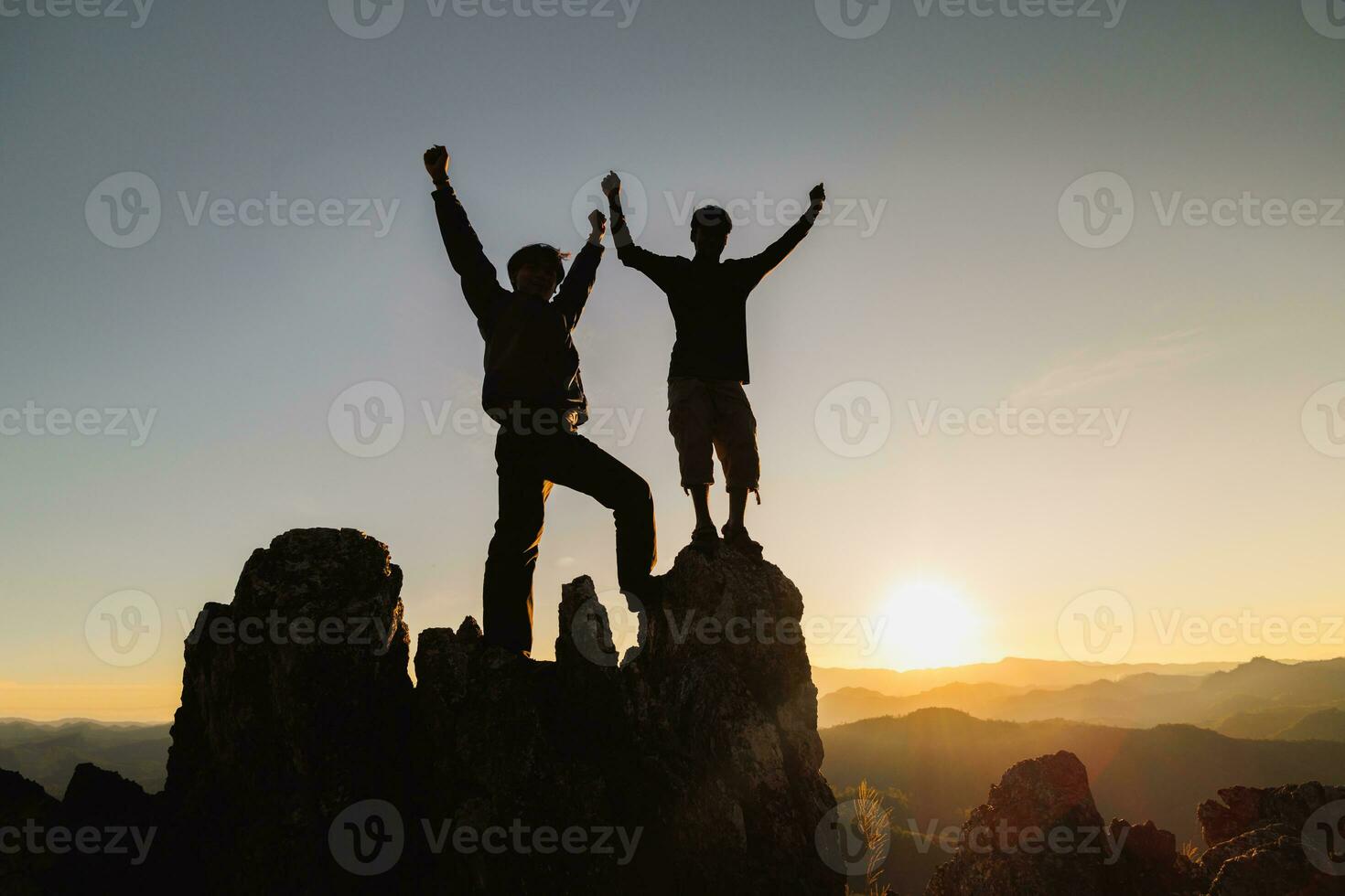Silhouette of two man with success gesture standing on the top of mountain. business teamwork concept. photo